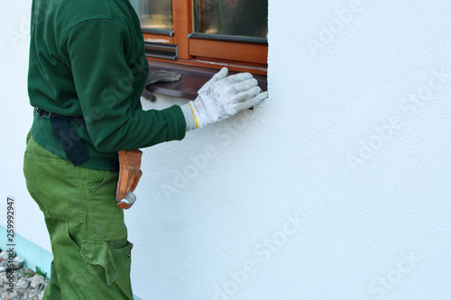 Wallpaper Mural Man worker in protective gloves installing sill on external wooden window frame on white house facade. Sill installation process. Exterior design, building, home improvement, diy concept. Torontodigital.ca