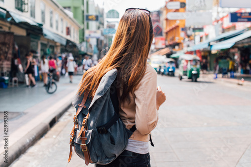 Rear view of young female tourist backpacker walking on Khao San road in summer during trip to Bangkok, Thailand