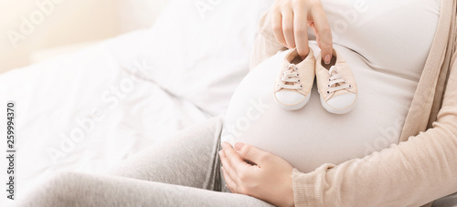 Small shoes for unborn baby on belly of pregnant woman photo