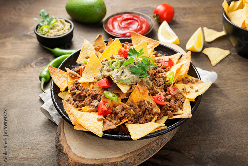 Corn chips nachos with fried minced meat and guacamole on wooden background. photo