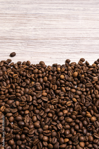 Roasted coffee beans in bulk on a light wooden background. dark cofee roasted grain flavor aroma cafe, natural coffe shop background, top view from above, copy space
