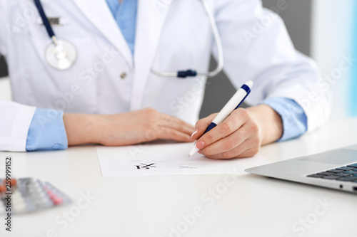 Female doctor filling up prescription form while sitting at the desk in hospital closeup.  Healthcare  insurance and excellent service in medicine concept 