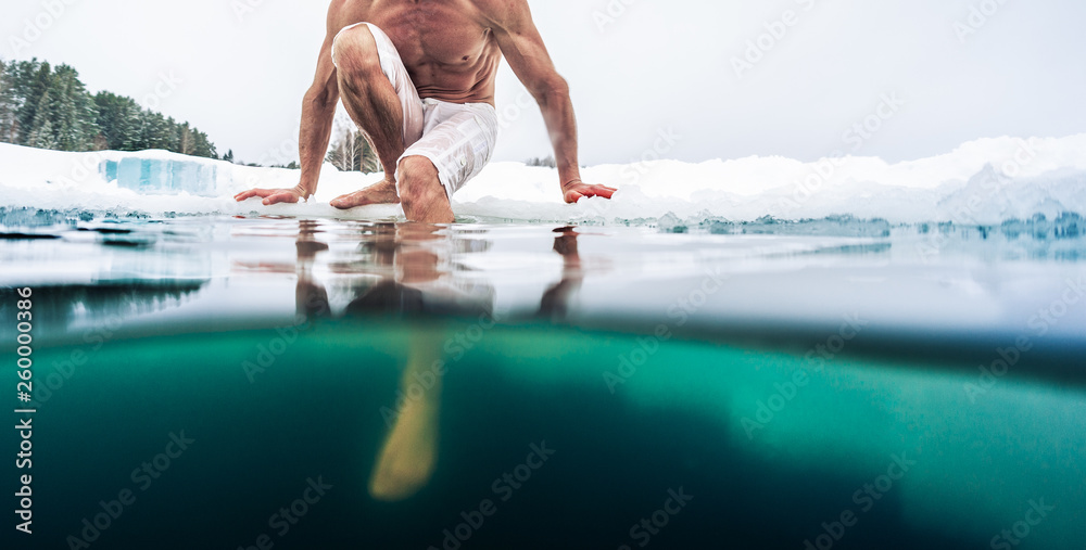 Young man with lean muscular body sits on the ice and going to swim in ...