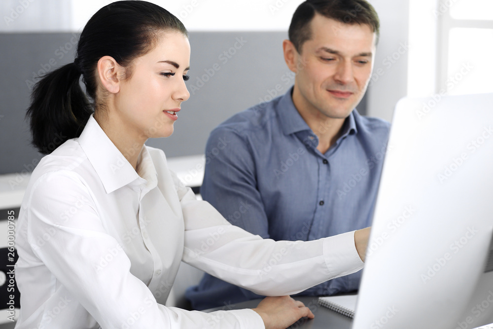 Cheerful smiling businessman and woman working with computer in modern office. Headshot at meeting or workplace. Teamwork, partnership and business concept 