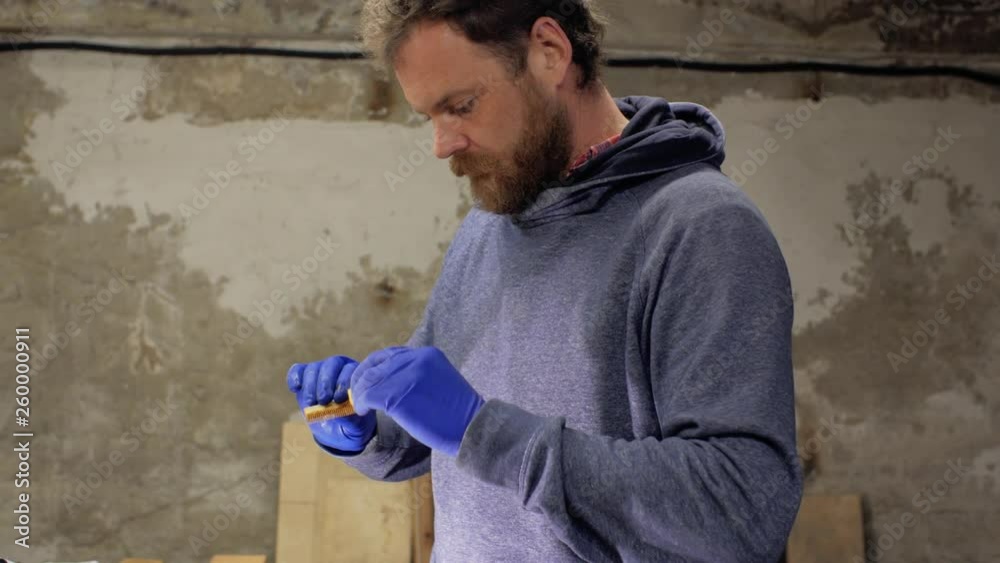 professional craftsman with a beard and mustache paints wood stain with a sponge indoors.wooden painting. 4 k professional craftsman with a beard and mustache paints wood stain with a sponge indoors.wooden painting. 4 k