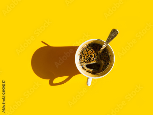 Foto White cup of freshly brewed coffee with foamy crema tea spoon on solid yellow background