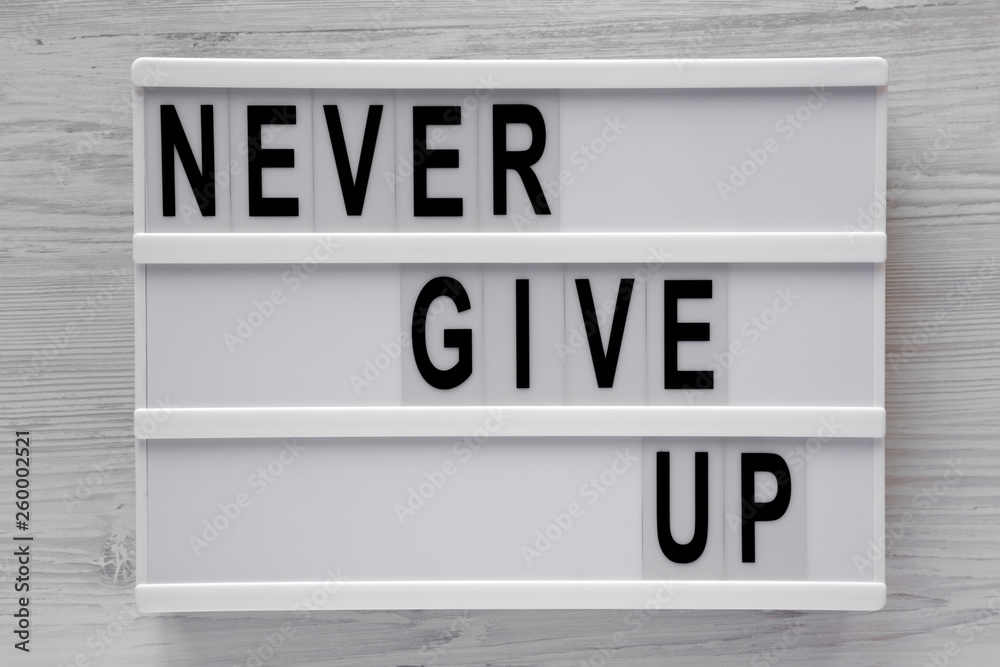 'Never give up' words on modern board over white wooden background. Flat lay, from above, overhead. Close-up. 'Never give up' words on modern board over white wooden background. Flat lay, from above, overhead. Close-up.