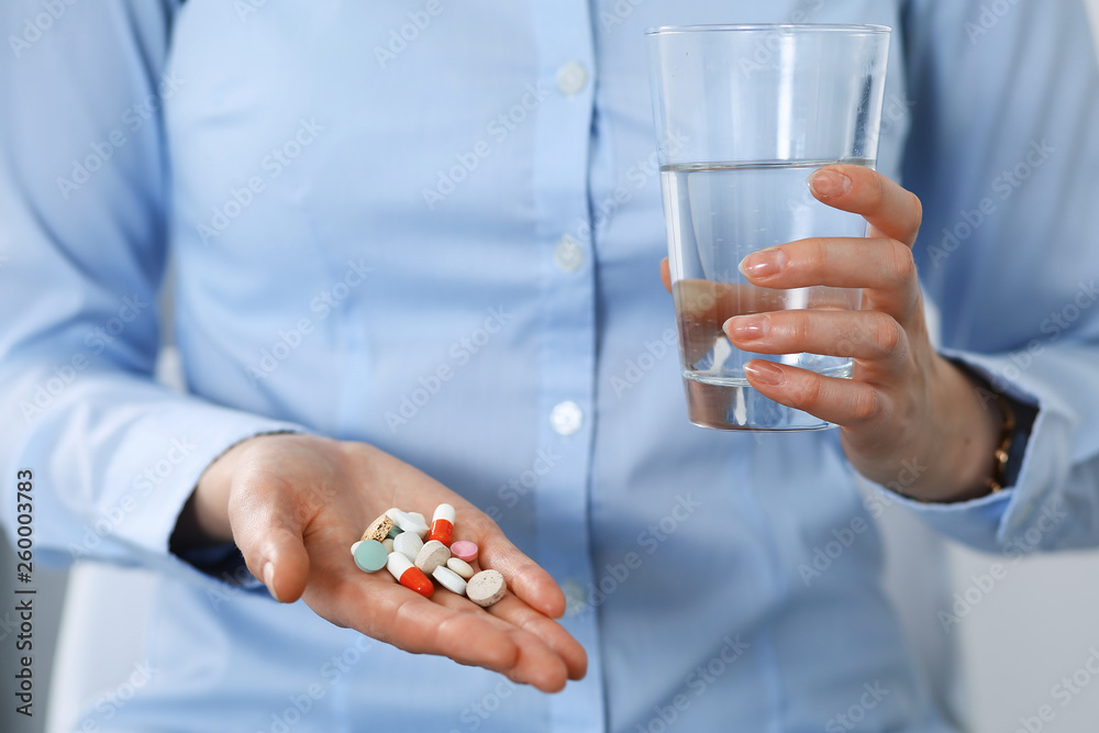 Young unknown woman holding pills and glass of water, closeup of hands. Medicine and healthcare concept Young unknown woman holding pills and glass of water, closeup of hands. Medicine and healthcare concept