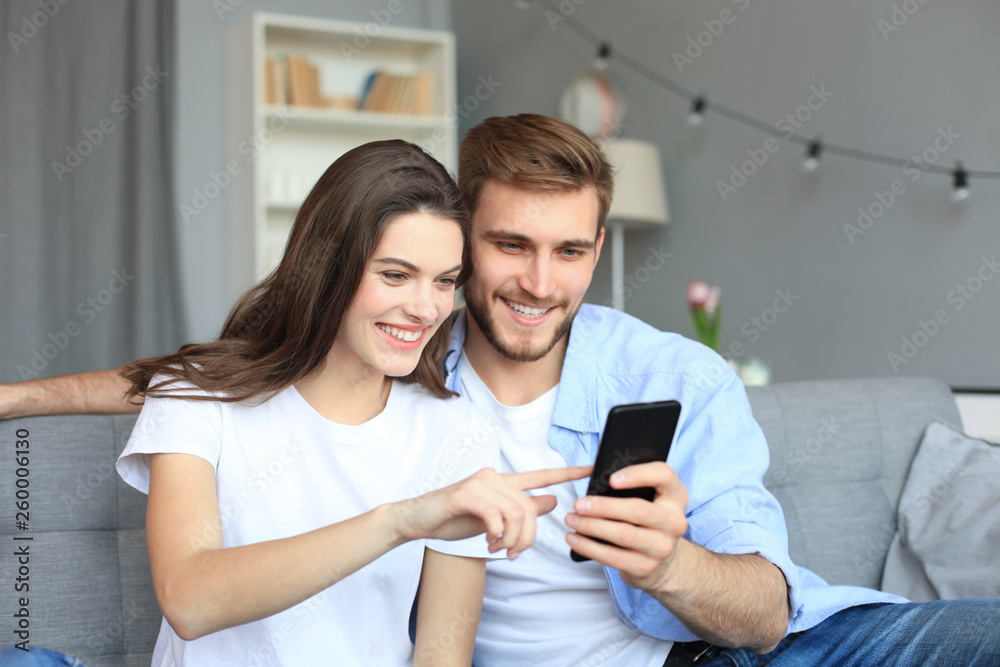 Young couple watching online content in a smart phone sitting on a sofa at home in the living room. Young couple watching online content in a smart phone sitting on a sofa at home in the living room.
