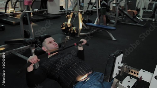 Cheerful fat man performs a wrong exercise in the gym. For the first time in a fitness club.