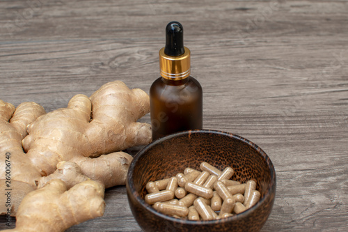 ginger root and oil bottle with dropper and ginger capsule in wooden bowl on wooden background, health care concept
