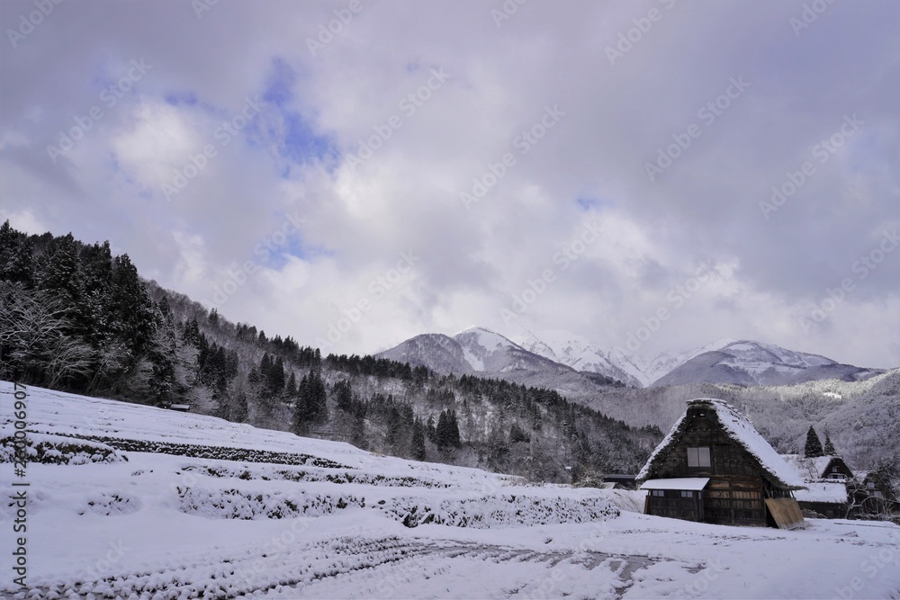 世界遺産の白川郷ー雪に覆われた山と田んぼ、右下に茅葺きの建物