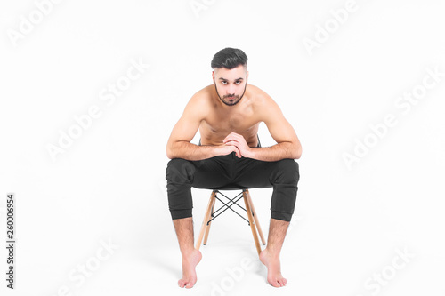 Attractive man with torso sitting on black chair in white studio. Lifestyle!