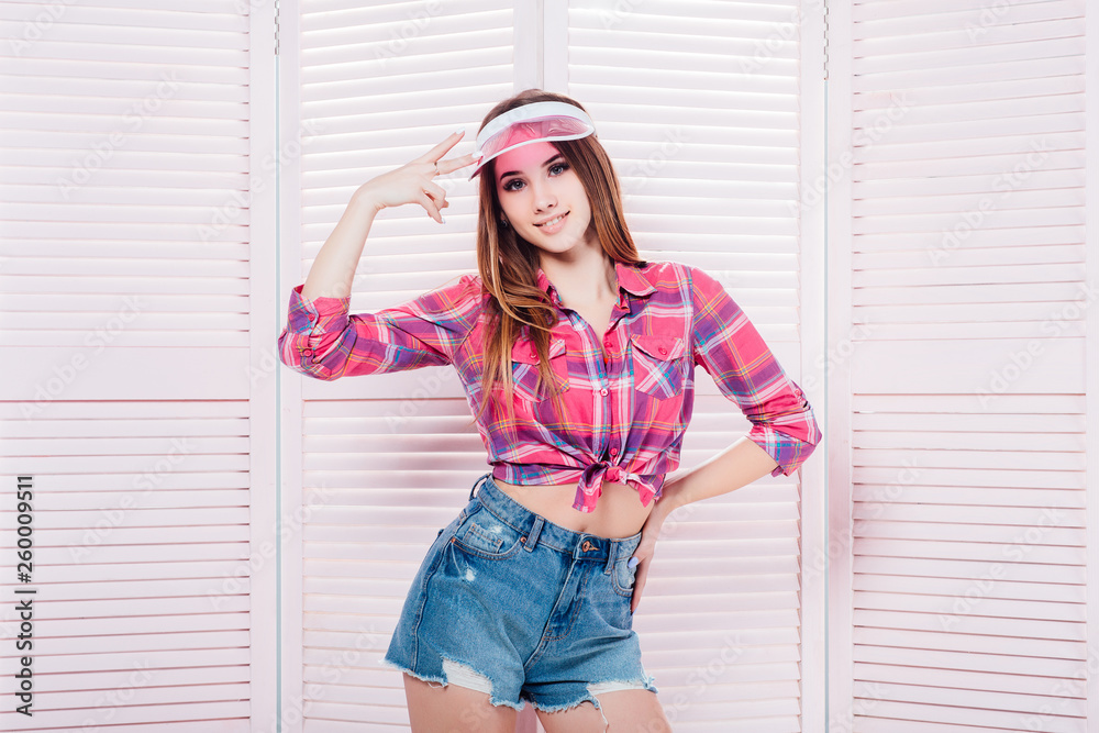 Pensive teen girl wearing checkered shirt and baseball cap looking up in thoughts over pink background, half length portrait