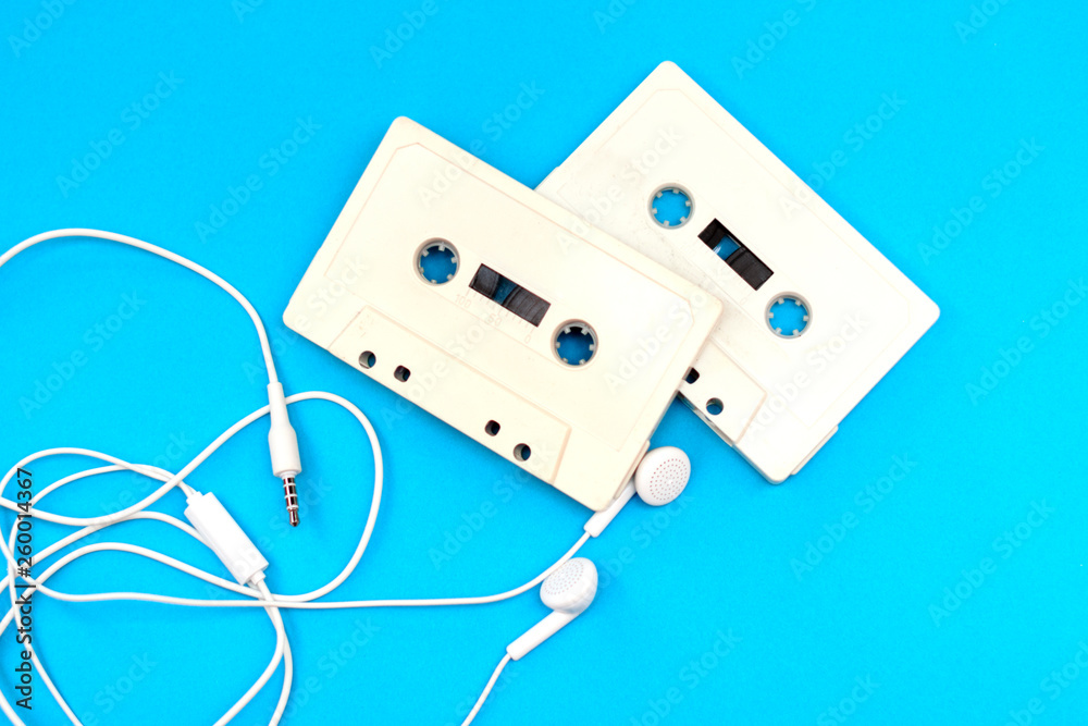 technology - old retro cassette tapes and new modern white headphones on blue background technology - old retro cassette tapes and new modern white headphones on blue background