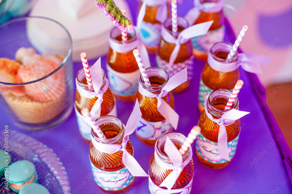 Birthday party concept, candy bar for children. A lot of bottles of apple juice, special labels on it, white and pink straws on purple background