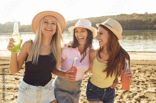 Young laughing girlfriends having drinks on beach