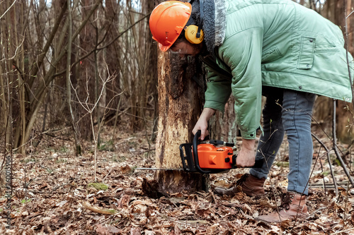 Logging, Worker in a protective suit with a chainsaw sawing wood. Cutting down trees, forest destruction. The concept of industrial destruction of trees, causing harm to the environment.