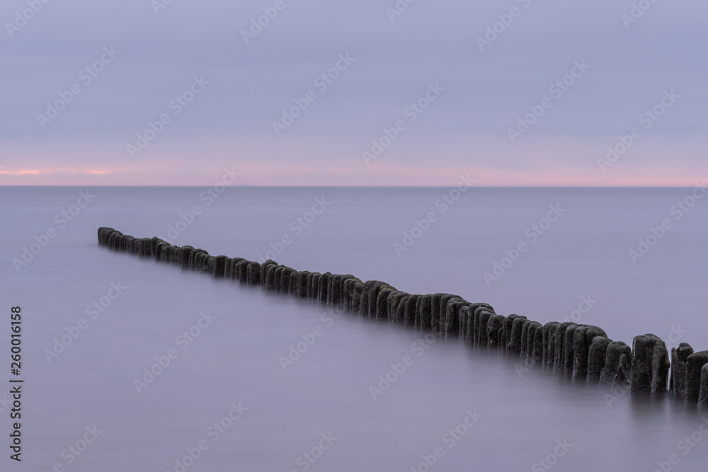 Fototapeta premium Long exposure photo of a wooden wavebreaker in the evening.