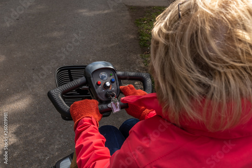 An over the shoulder shot of an elderly lady in a red coat enjoying the freedom of an electric mobility scooter.