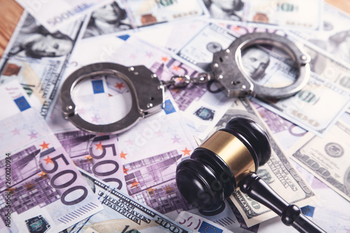 Metallic handcuffs with money and judge gavel.