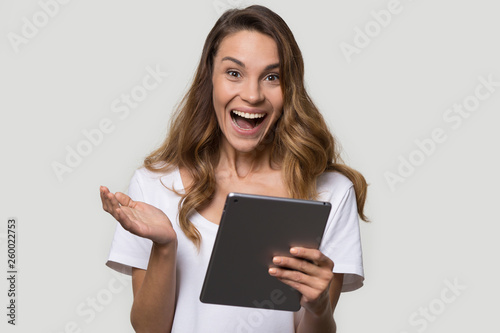 Amazed woman holding digital tablet looking at camera feels happy
