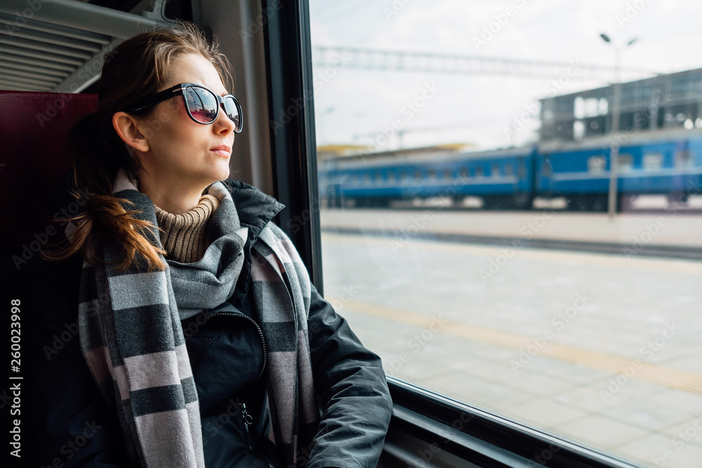 Fototapeta premium Young woman wearing travel glasses, looking out the window, sitting in train