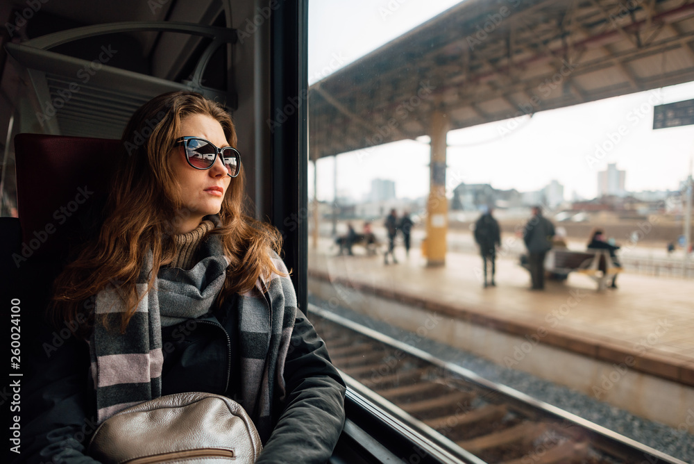 Young woman wearing travel glasses, looking out the window, sitting in train