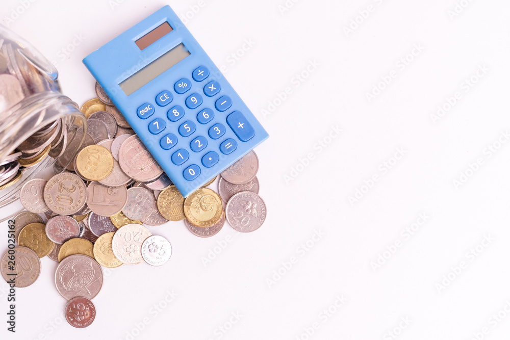 Coins in glass jar with blue mini calculator on white background isolated. Financial and economy concept. Coins in glass jar with blue mini calculator on white background isolated. Financial and economy concept.