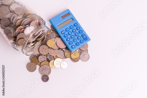 Coins in glass jar with blue mini calculator on white background isolated. Financial and economy concept.