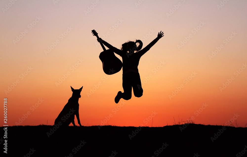 Silhouette girl guitarist on sunset background, silhouette of a dog breed Belgian Shepherd Malinois, happy friends, outdoor, jumping 