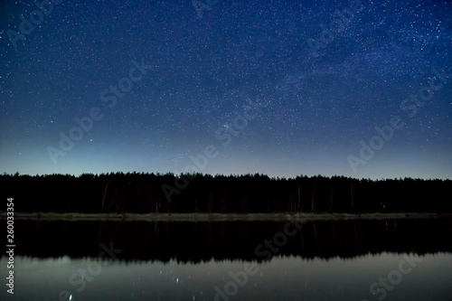 Wonderful beautiful night sky full of stars with Milky way over the river and forest in transparent april night