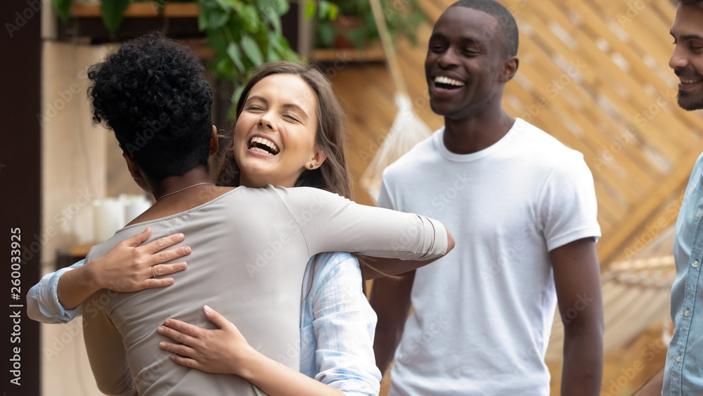 Happy caucasian teen girl embracing african friend at group meeting - obrazy, fototapety, plakaty 