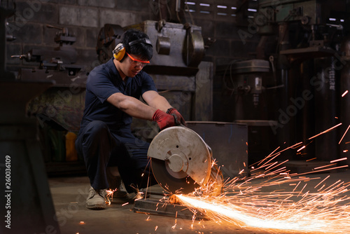 Asian workshop engineer operating an abrasive cut-off saw with metal sparks - Hispanic production technician cutting metal using power tools in a dark factory