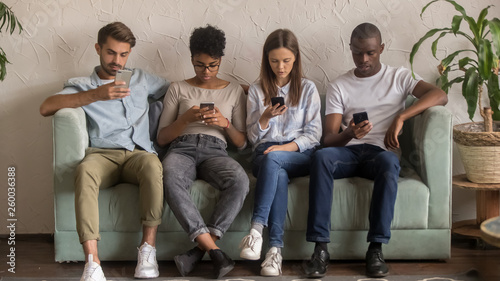 Multicultural people using smartphones ignoring each other sitting on sofa