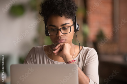 Focused african american girl student wearing headphones looking at laptop photo
