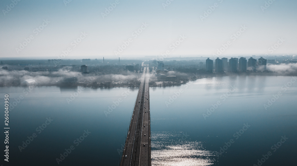 Fototapeta premium Aerial view of fog or mist over Voronezh river and North Bridge with car traffic, panoramic drone shote from above, morning haze and cityscape