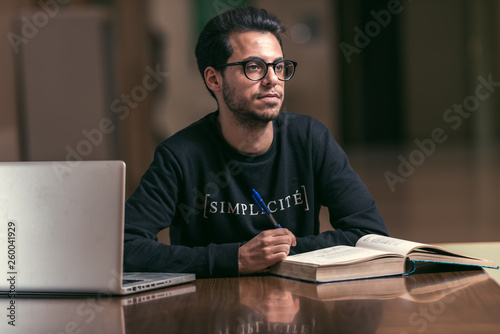 Fotografie Young computer science student use a laptop and a large book to study at the Polytechnic School in Caceres, Spain