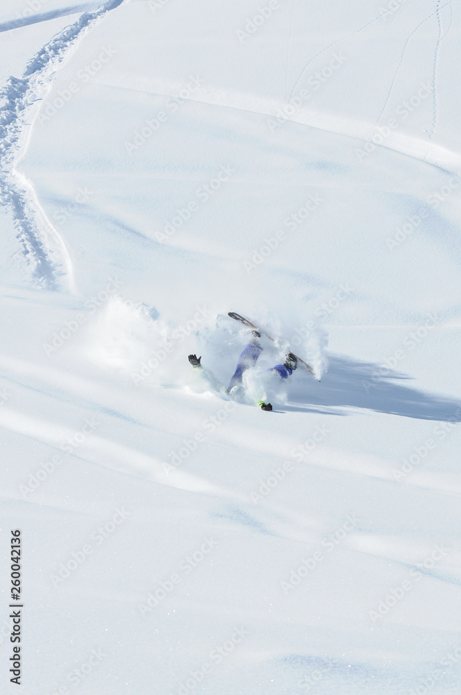 A snowboarder falling into deep snow at the ski resort in a sunny morning