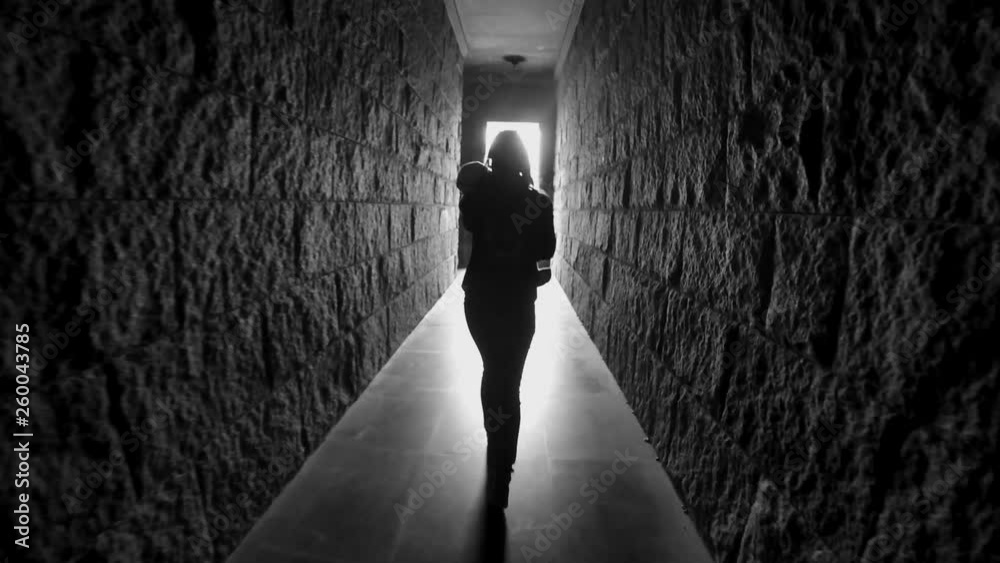 girl with long hair walks down a dark corridor tunnel with her back