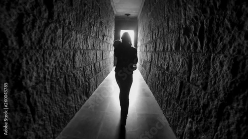 girl with long hair walks down a dark corridor tunnel with her back