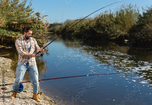 Adult man standing near river and pulling fish expressing emotions of dedication