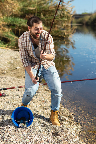 Adult man standing near river and pulling fish expressing emotions of dedication