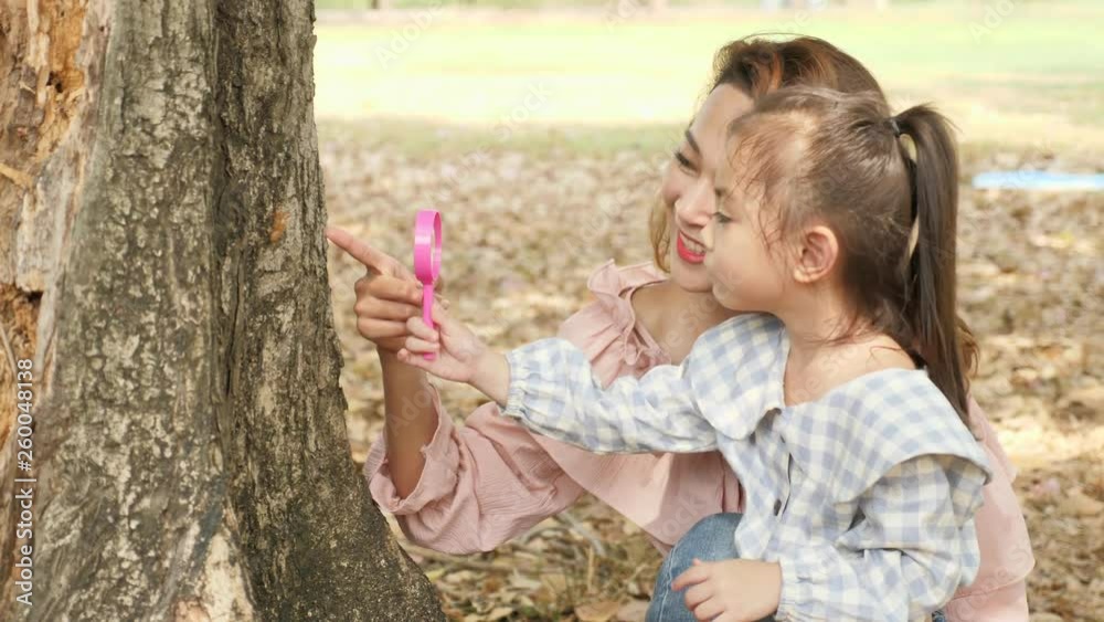 Mother with daughter looking at tree bark through magnifying glass in the park Mother with daughter looking at tree bark through magnifying glass in the park