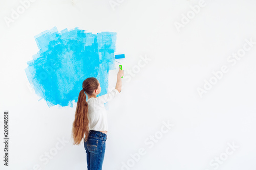 Repair in the apartment. Happy child girl paints the wall with blue paint,