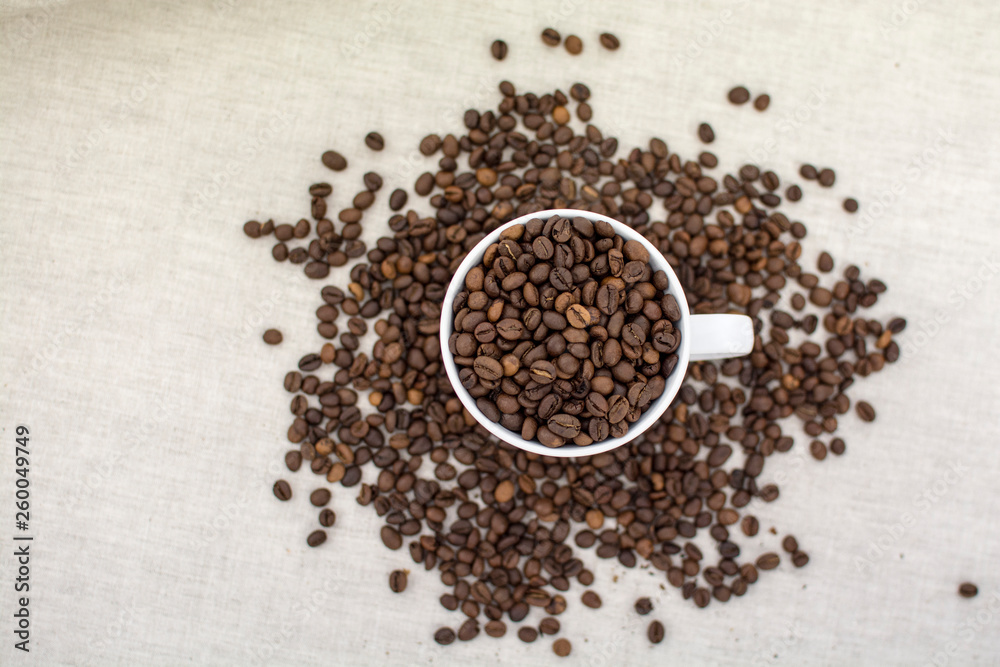 Coffee beans covered in a white Cup and scattered next to the linen fabric Coffee beans covered in a white Cup and scattered next to the linen fabric