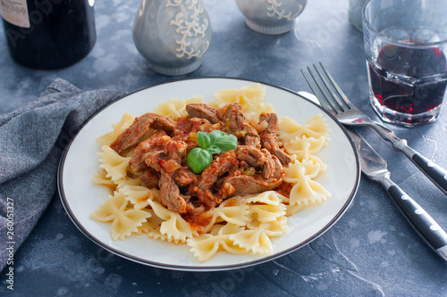 Beef in tomato sauce with farfalle on a white plate, horizontal