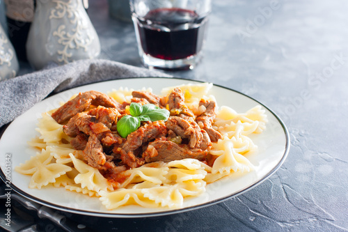 Beef in tomato sauce with farfalle on a white plate, horizontal, copy space