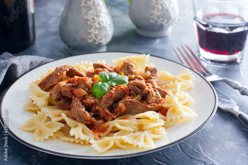 Beef in tomato sauce with farfalle on a white plate, horizontal