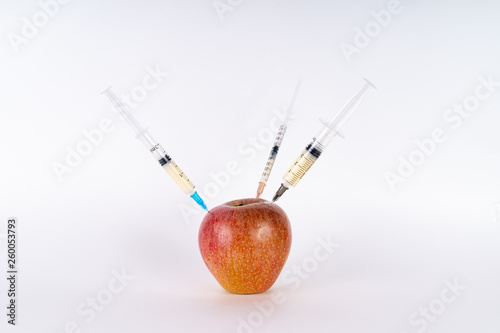 Injection of a red apple with three syringes. Antibiotic or GMO. Genetically modified fruits on white background
